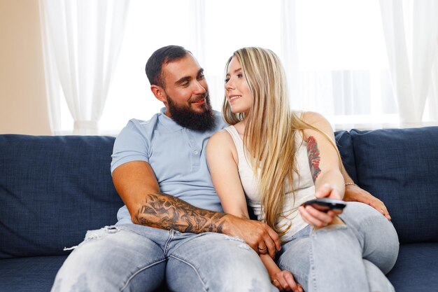 Feliz pareja sonriente sentada en un sofá azul en la sala de estar