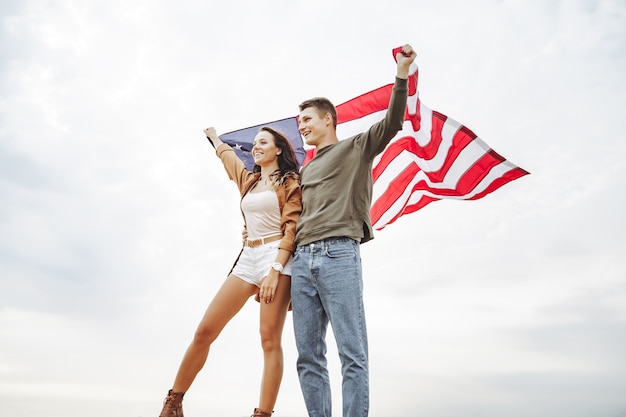 Feliz pareja sosteniendo la bandera americana en la naturaleza