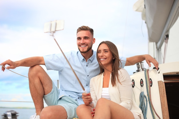 Feliz pareja tomando un selfie después de la propuesta de compromiso en velero, relajándose en un yate en el mar.