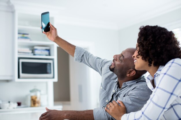 Feliz pareja tomando selfie en teléfono móvil en la sala de estar