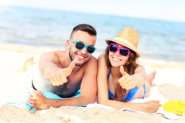 Feliz pareja tumbada en la playa y mostrando signos de ok