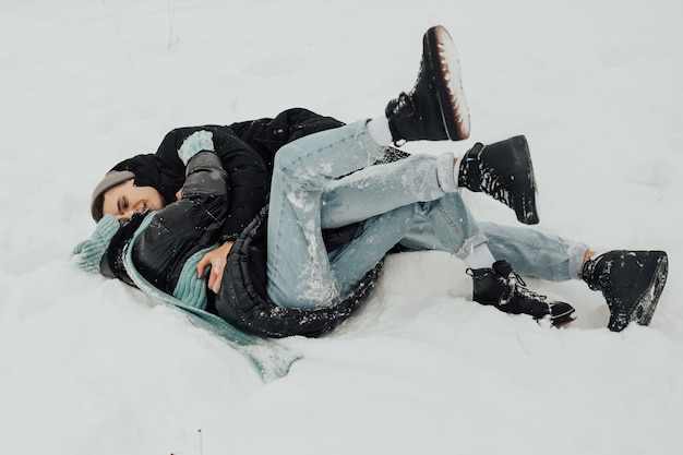 Feliz pareja tumbado en la nieve se ríen y abrazan