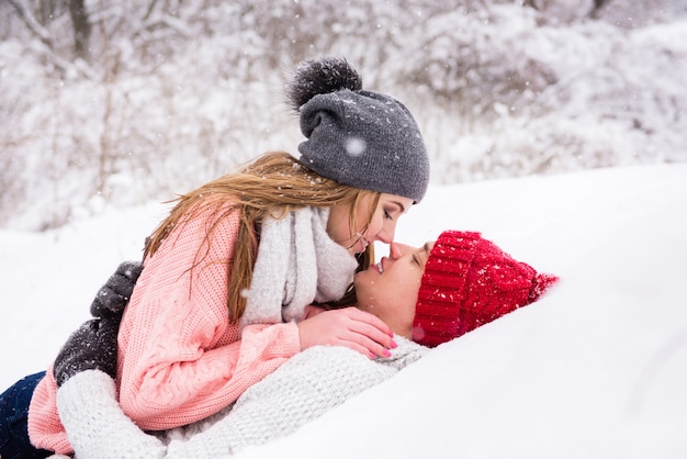 Feliz pareja tumbarse y besarse en la nieve