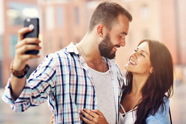 Feliz pareja de turistas con smartphone en ciudad en día lluvioso