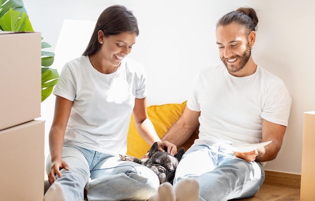 Feliz pareja uniéndose con perro en casa nueva leyendo contrato