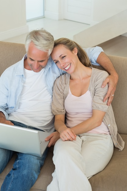 Feliz pareja usando la computadora portátil juntos en el sofá