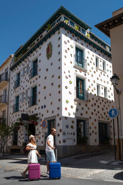 Feliz pareja de vacaciones con maletas en un pueblo andaluz con arquitectura típica y colorida