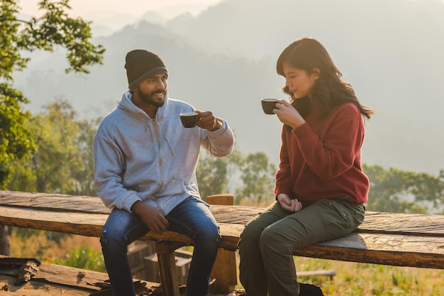 Feliz pareja de viajeros descansando en las montañas al amanecer tomando café