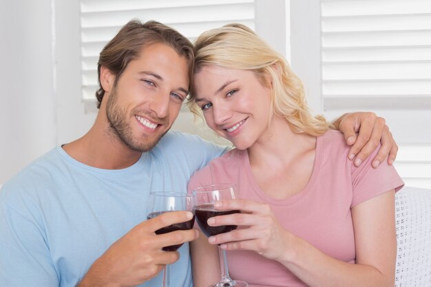 Feliz pareja con vino tinto en el sofá