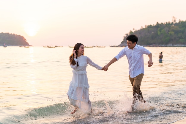 Feliz pareja yendo de viaje de luna de miel en la playa de arena tropical en verano