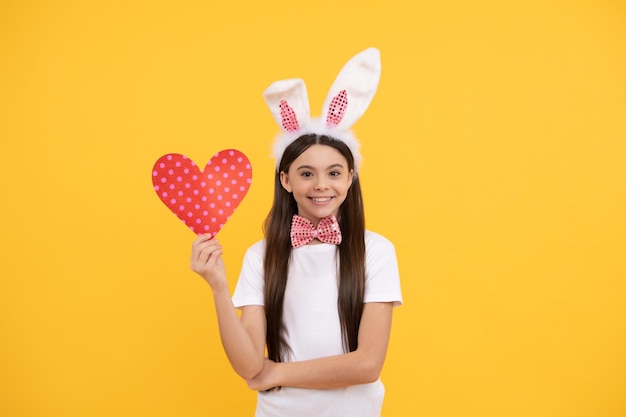 Feliz páscoa adolescente em orelhas de coelho e gravata borboleta segura coração de amor feriado de páscoa