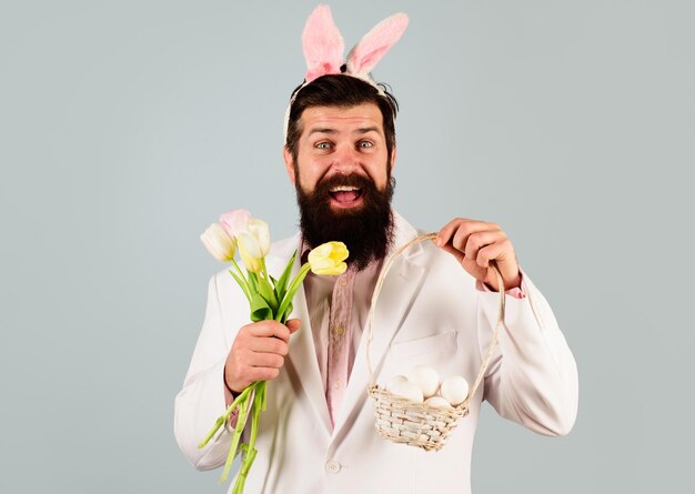 Feliz páscoa coelho homem em orelhas de coelho com flores e ovos de cesta cara feliz de terno com tulipas