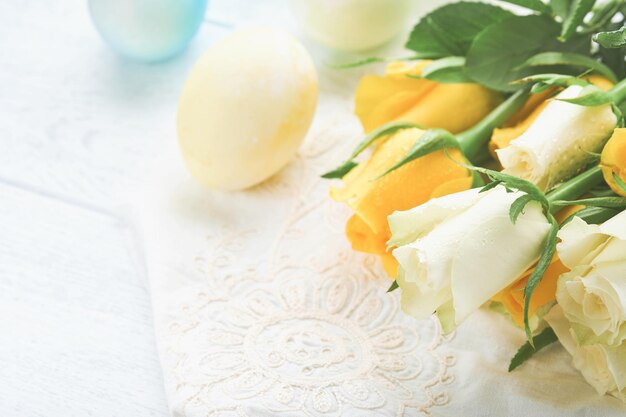 Feliz Páscoa Ovos de Páscoa na mesa rústica com rosas brancas e amarelas Ovos coloridos tingidos naturais em placa de madeira e flores de primavera em sala rústica Imagem tonificada Fundo de Páscoa com espaço de cópia