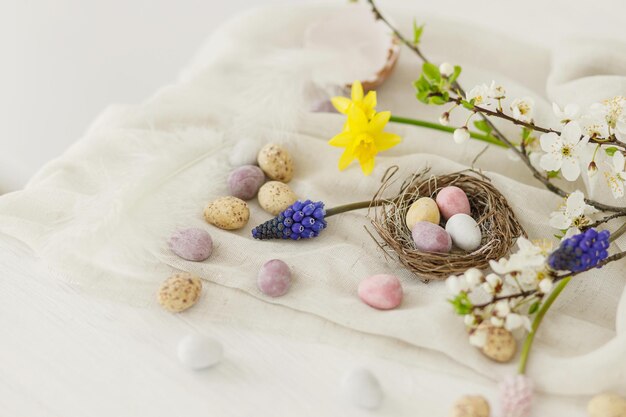 Feliz Páscoa Páscoa elegante ovos de chocolate em ninho flores de primavera penas e pano de linho em branco mesa de madeira rústica Páscoa moderno simples banner espaço para texto saídas de estações