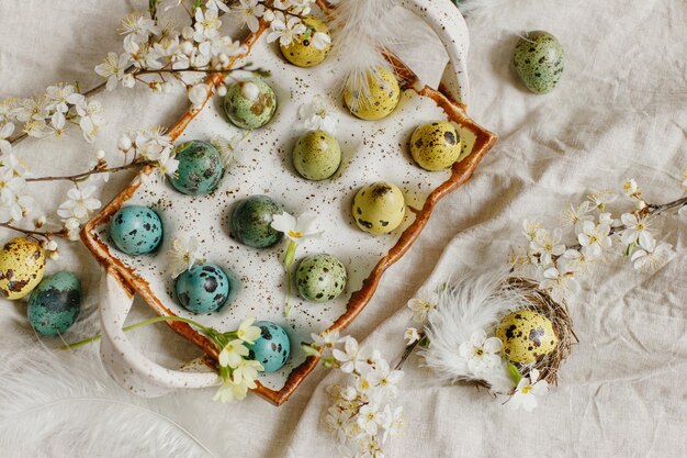 Feliz Páscoa Páscoa rústica plana Ovos de Páscoa elegantes e flores de primavera florescendo na mesa rústica Ovos de codorna pintados naturais em penas de bandeja e flores de cerejeira em tecido de linho