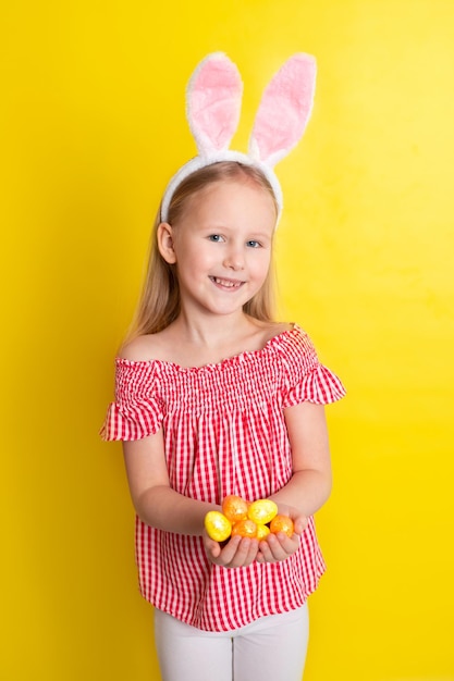 Feliz Páscoa Uma linda garota com orelhas de coelho segura ovos coloridos nas mãos e sorri alegremente fundo amarelo Espaço para texto Foto de alta qualidade