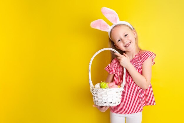 Feliz Páscoa Uma linda garota com orelhas de coelho segura ovos coloridos nas mãos e sorri alegremente fundo amarelo Espaço para texto Foto de alta qualidade