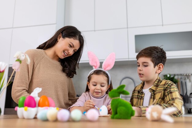 Foto feliz páscoa uma mãe filho e sua filha pintando ovos de páscoa família feliz se preparando para a páscoa menina bonita usando orelhas de coelho no dia de páscua