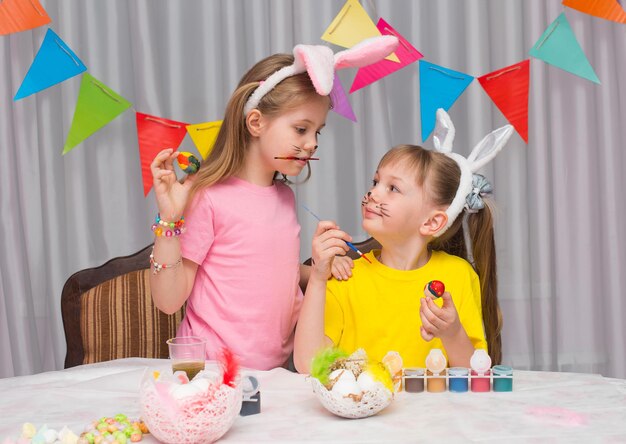 Foto feliz pascua chicas con orejas de conejo divirtiéndose pintando huevos preparándose para la pascua
