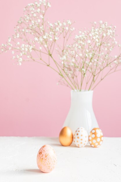 Feliz Pascua decoración de interiores. Tres huevos de oro y gypsoghila en flor blanca en la pared rosa