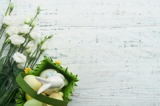 Feliz Pascua Huevos de Pascua y conejo en canasta verde sobre una mesa de madera vieja blanca con rosas blancas y amarillas Tarjeta de vacaciones de Pascua feliz de primavera Fondo de Pascua con espacio de copia Vista superior