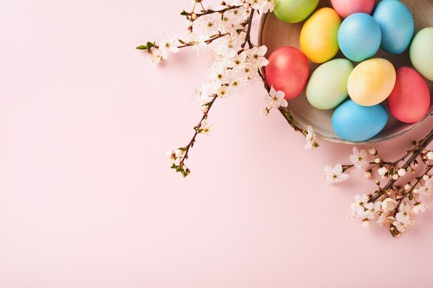 Feliz Pascua Huevos de Pascua teñidos en mesa rústica con rama de cerezo en flor sobre fondo rosa Fondo de tarjeta de vacaciones de Pascua con espacio de copia Vista superior