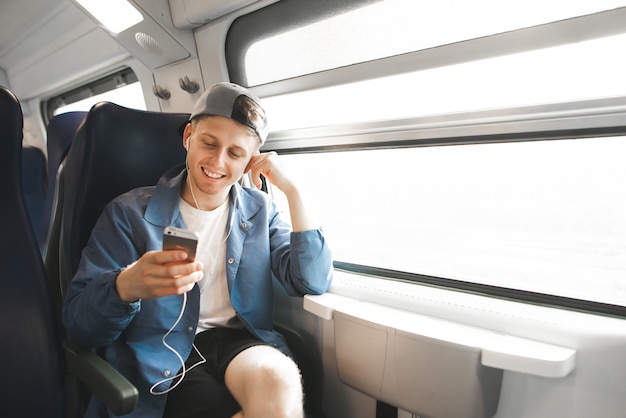 Feliz passageiro está sentado no trem perto da janela e usa a internet no smartphone