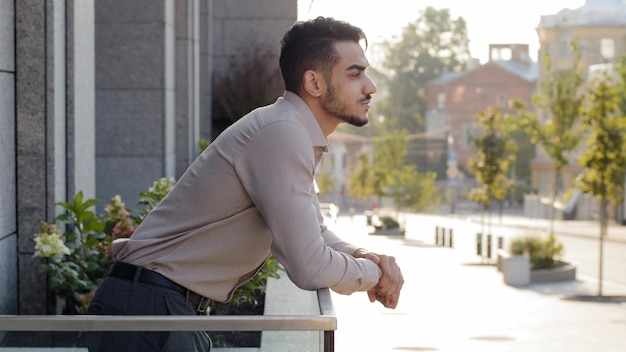 Feliz pensativo exitoso hombre de negocios relajado hombre hispano hombre inversionista árabe hombre de negocios se encuentra en el balcón de la terraza en el edificio de oficinas en la habitación del hotel en casa pensando mirando el paisaje urbano disfrutar de la vista