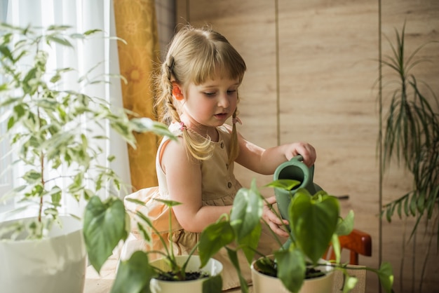 Feliz pequena menina bonita cuida de plantas de casa. Menina regando e pulverizando plantas de interior em casa