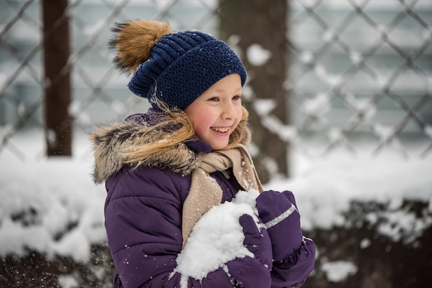 Feliz pequeña niña rubia divirtiéndose jugando con nieve en día de invierno