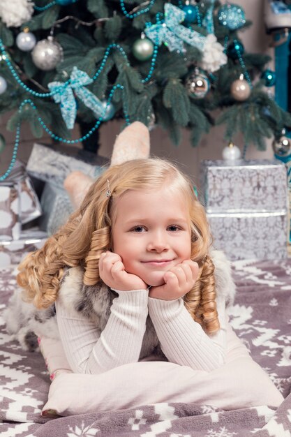 Feliz pequeña niña en vestido con presente tiene una Navidad