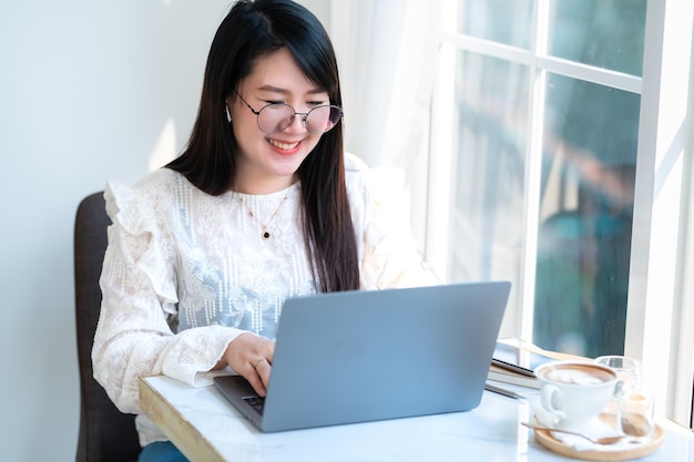 Feliz de personas independientes asiáticas Mujer de negocios que usa auriculares inalámbricos trabajando casualmente con una computadora portátil con una taza de café Cuaderno y teléfono inteligente en el caféComunicación de estilo de vida empresarial