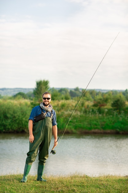 Feliz pescador con traje especial y caña de pescar cerca del río