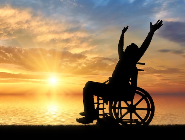 Feliz pessoa com deficiência em uma cadeira de rodas com os braços levantados em um fundo por do sol do mar. O conceito de pessoas felizes com deficiência