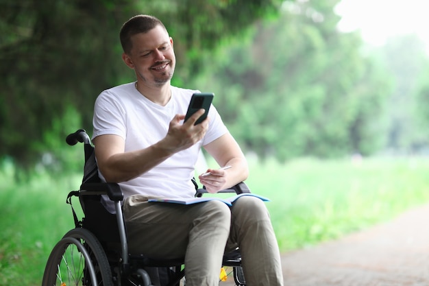 Feliz pessoa com deficiência senta-se na cadeira de rodas no parque e conversa ao telefone.