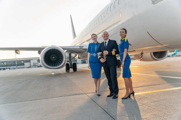 Feliz piloto y asistentes de vuelo de pie junto al gran avión juntos