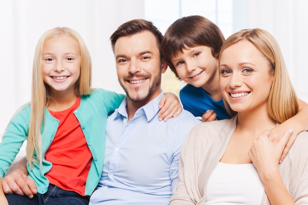 Foto feliz por ser uma família. família feliz de quatro pessoas se unindo e sorrindo enquanto estão sentados dentro de casa