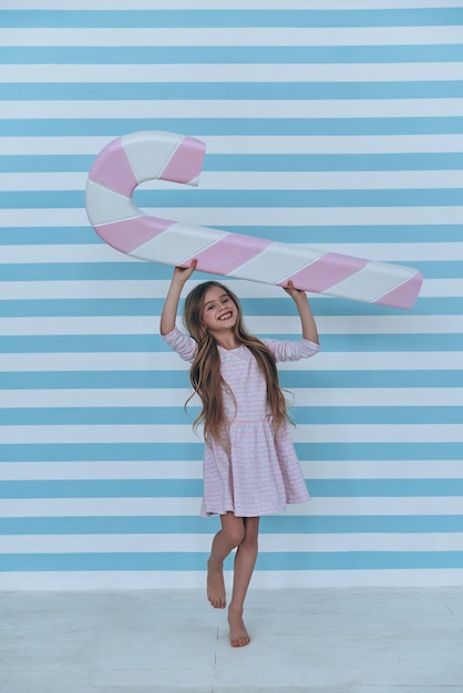 Feliz por ter um doce. Menina adorável olhando para a câmera e sorrindo