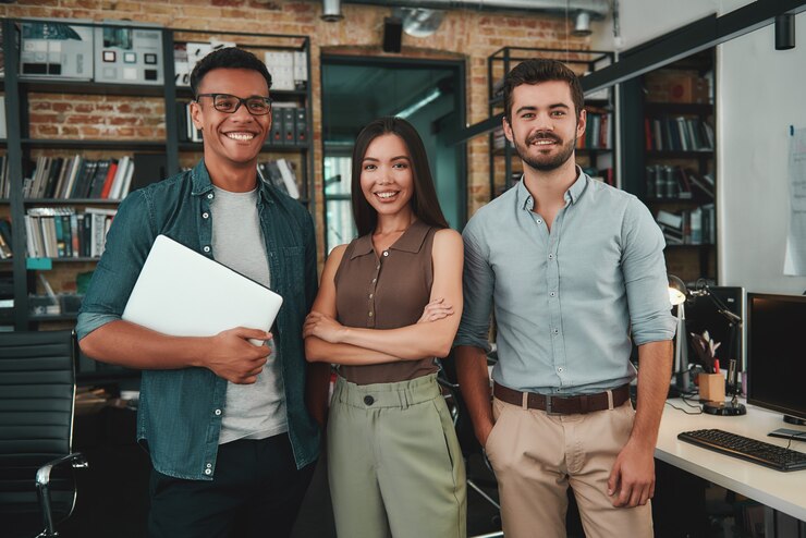Feliz por trabalhar junto com um grupo de três jovens alegres em roupas casuais olhando para
