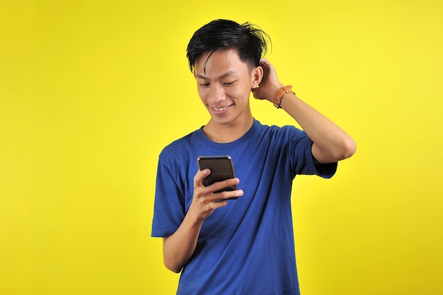 Feliz por um jovem asiático bonito sorrindo usando smartphone isolado em fundo amarelo