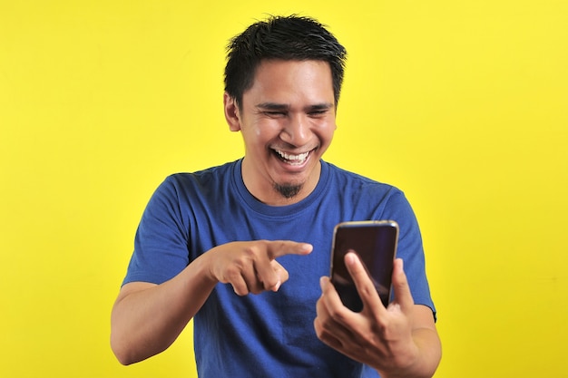 Feliz por um jovem asiático bonito sorrindo usando smartphone isolado em fundo amarelo