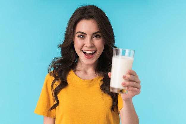 feliz positivo optimista joven hermosa mujer posando aislada sobre pared azul con leche.