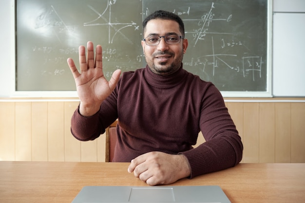 Feliz professor de raça mista cumprimentando alunos on-line no local de trabalho