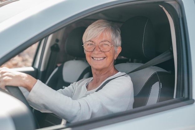 Foto feliz proprietário mulher madura bonita sentada relaxada em seu carro recém-comprado olhando pela janela sorrindo alegremente um velho sênior dirigindo e se divertindo