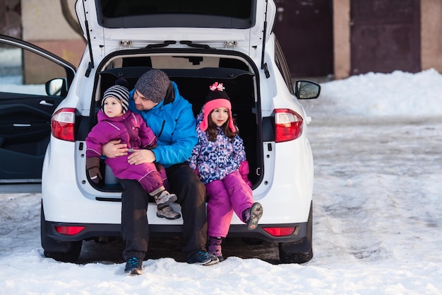 Feliz ramily, padre con niños sentado en el maletero del coche en invierno