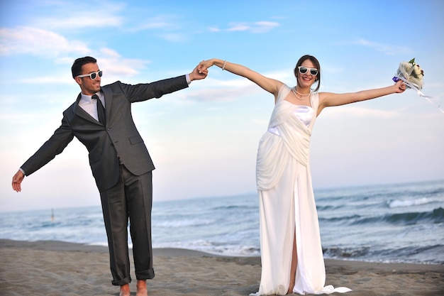 feliz recém casado jovem casal comemorando e se divertindo no belo pôr do sol da praia