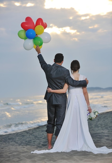 feliz recém casado jovem casal comemorando e se divertindo no belo pôr do sol na praia