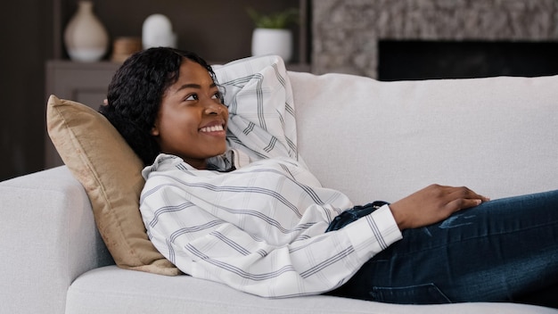 Feliz relajado salón de descanso de mujer afroamericana acostado en el sofá disfrutar de un estado de ánimo tranquilo informal de fin de semana