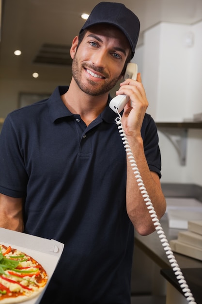 Feliz repartidor de pizza tomando un pedido por teléfono