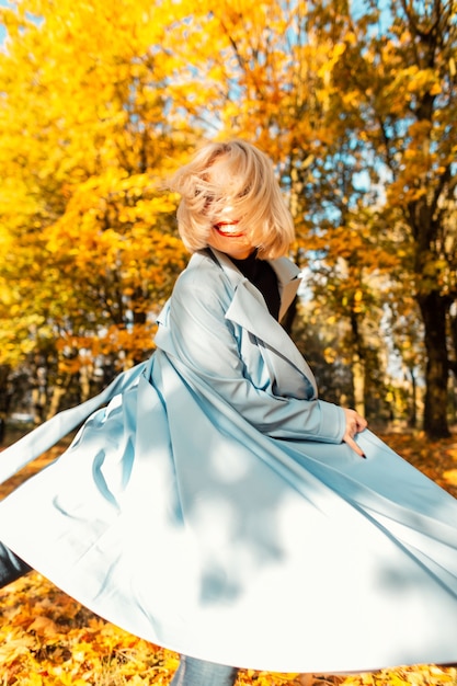 Feliz retrato creativo de una joven sonriente hermosa divertida con un abrigo de moda camina en movimiento en un parque otoñal con follaje de colores brillantes. Emociones alegres y positivas de las mujeres.